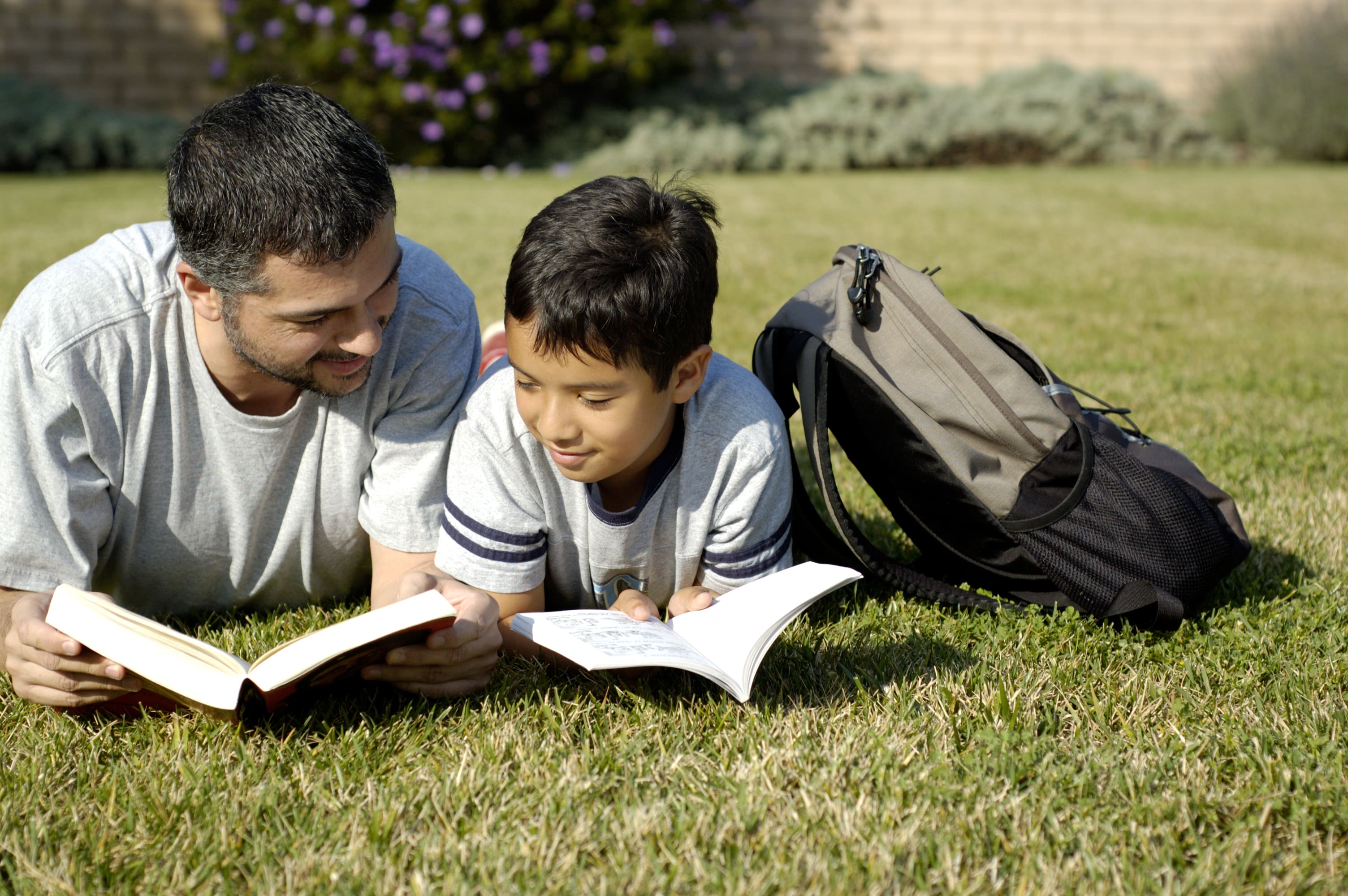 Father and son reading each others books at the park.