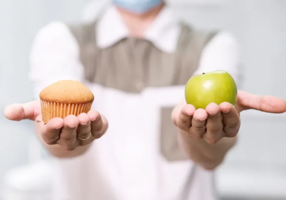 A person holding an apple and cupcake in their hands.